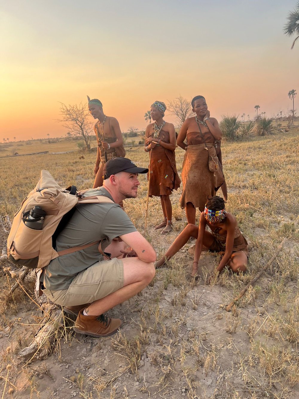 Callum crouching in the bush with a group of indigenous San people at sunset