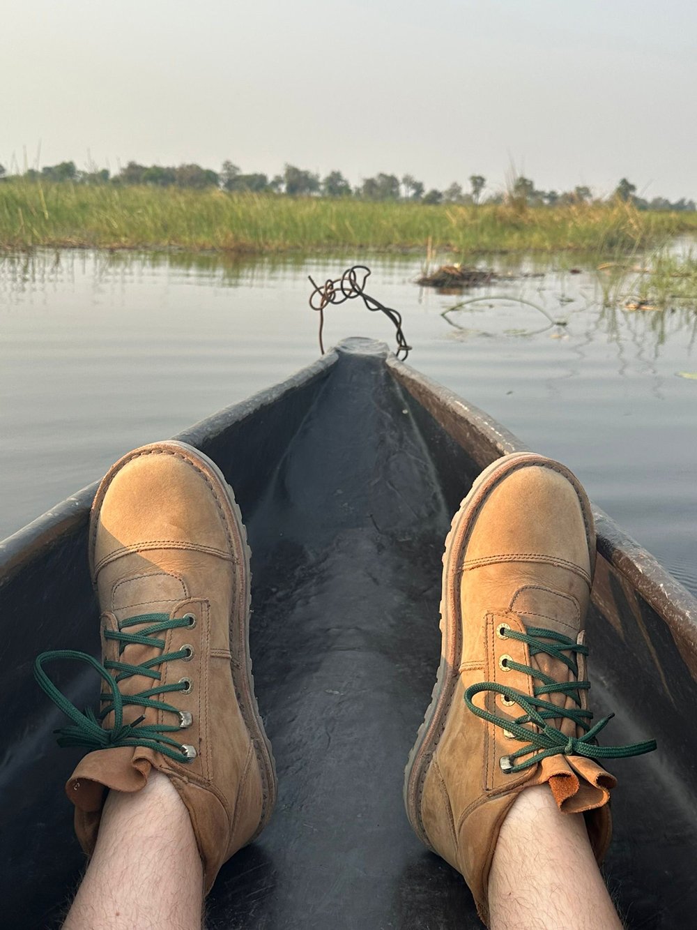 Person wearing Jim Green boots resting their feet on the bow of a mokoro canoe on a river